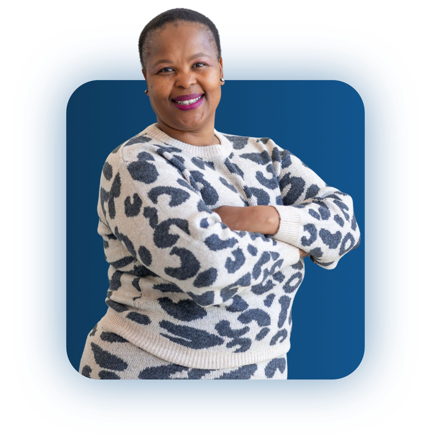 Smiling woman with crossed arms wearing a beige and gray leopard print sweater against a blue background.
