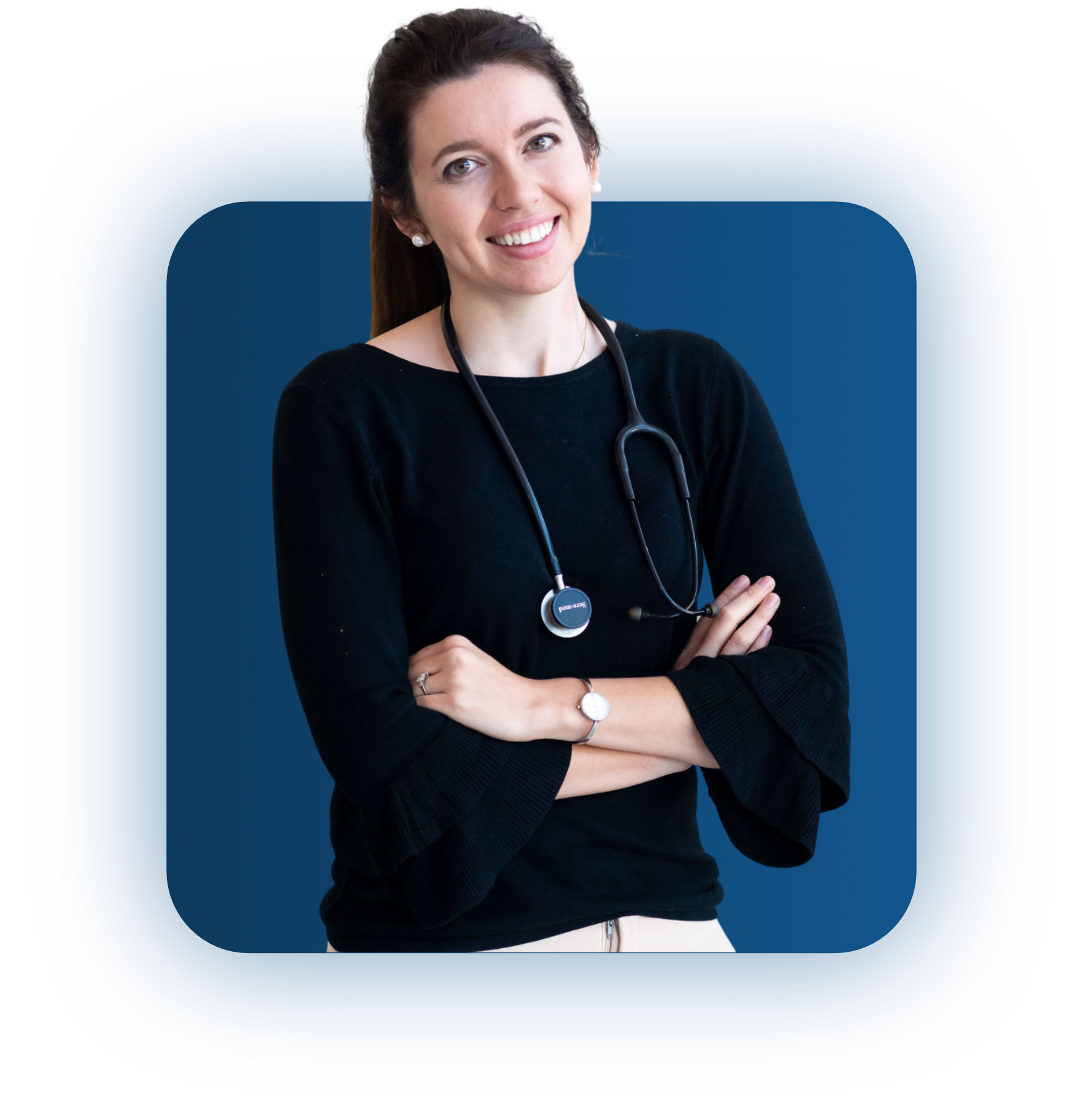 Smiling woman wearing a black sweater with ruffled sleeves and a stethoscope around her neck standing with arms crossed against a blue background.