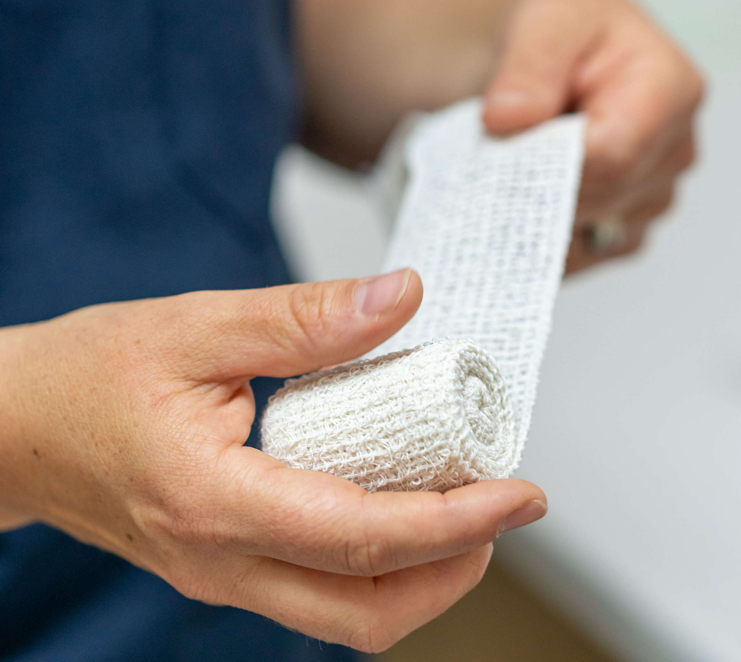 Person holding and unrolling a white medical gauze bandage wrap.