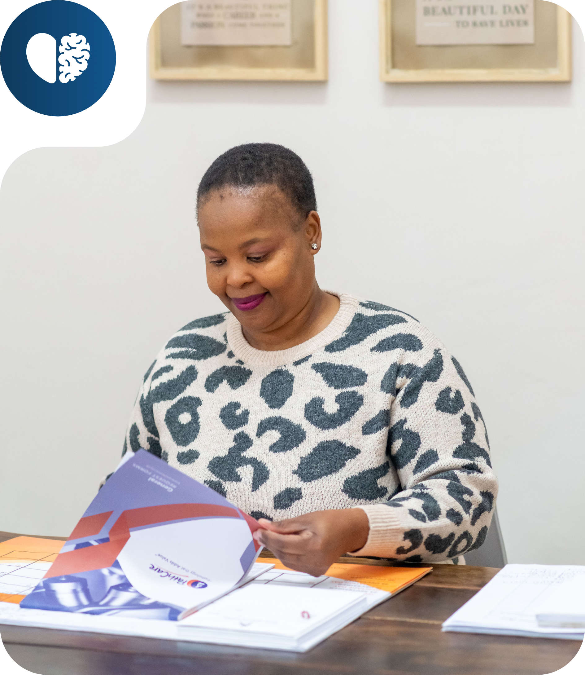 Woman in a leopard print sweater sitting at a table, reading a booklet with documents spread out.